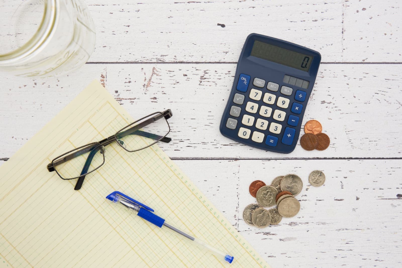 A calculator, coins and a ledger notebook on a desk
